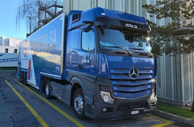 Un semi-camion blanc roule sur une route avec des montagnes en arrière-plan.