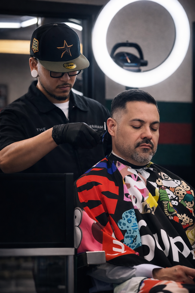 Barber cuts a client’s hair in a modern shop with a glowing ring light.