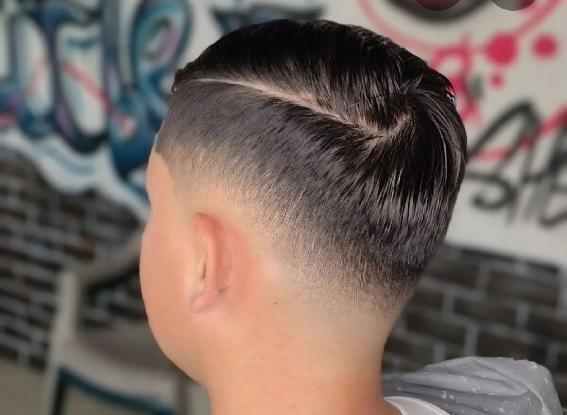 Short faded haircut with dark hair, viewed from the back against a graffiti wall.