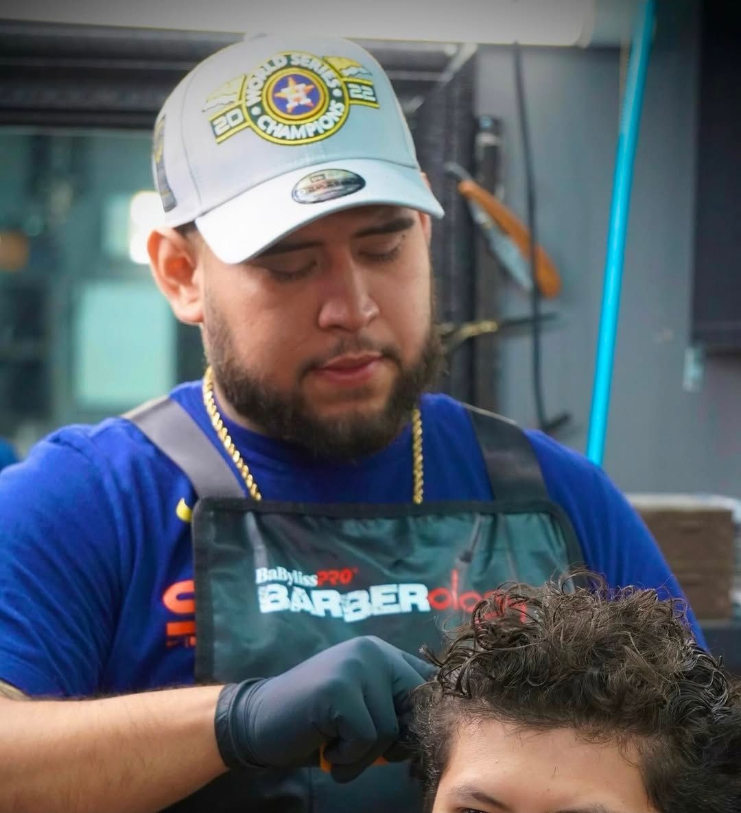 Barber in blue shirt and apron trims a customer’s hair with clippers in a salon.
