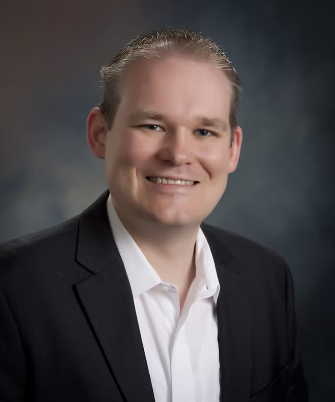 Studio portrait of a smiling man in a dark suit jacket and white shirt