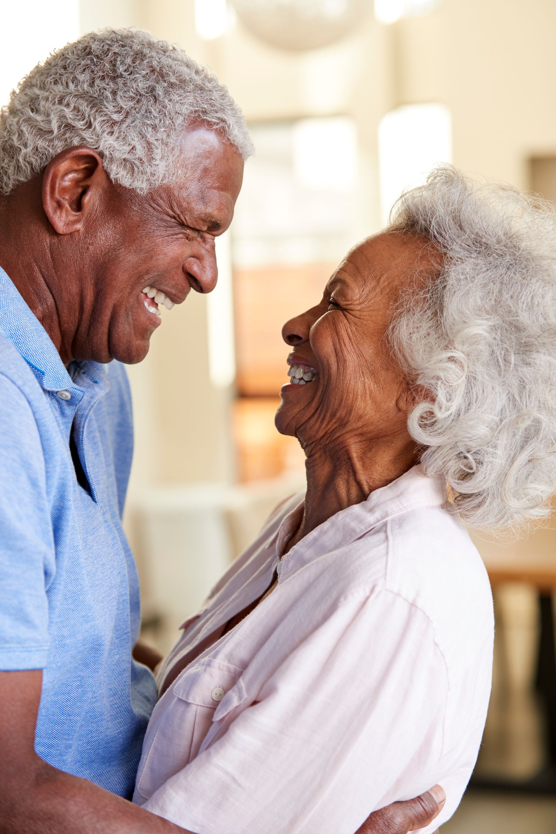 An elderly couple is sitting in a chair and smiling for the camera.