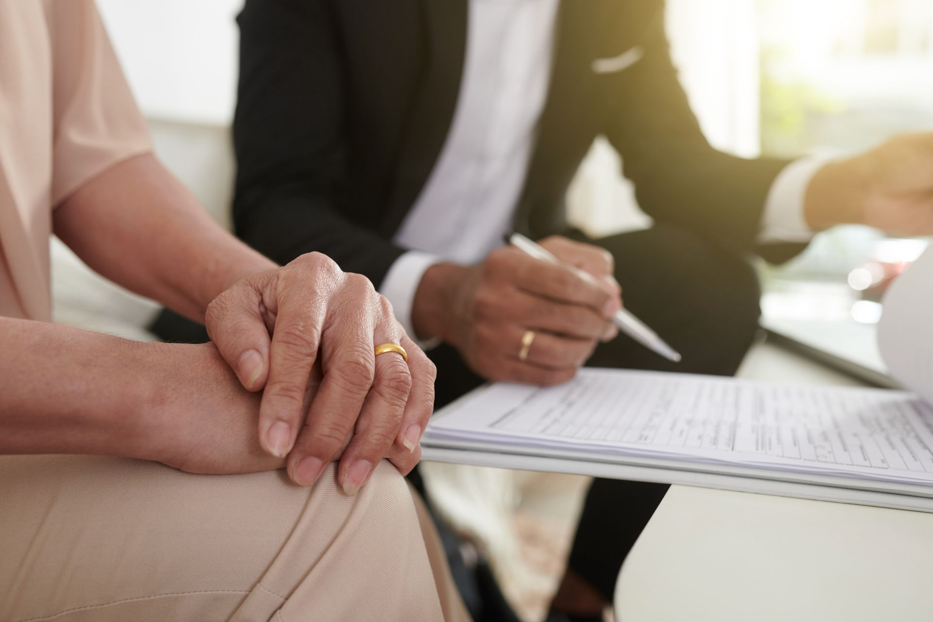 Hands clasped beside a person signing paperwork at a table.