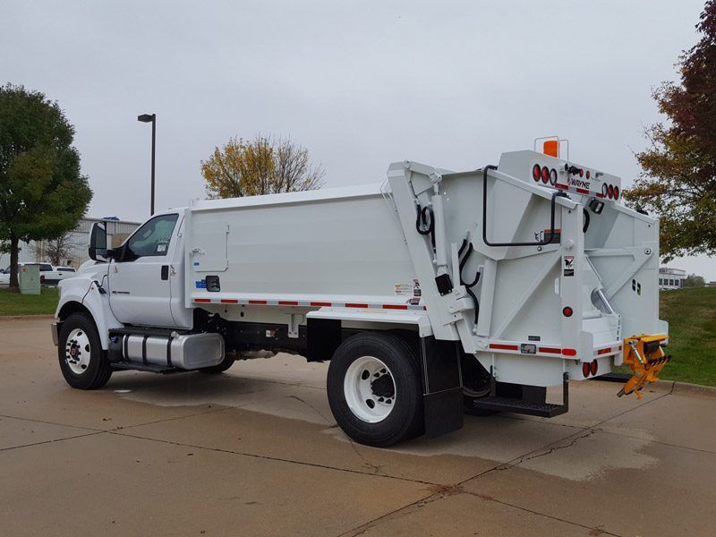 White dump truck parked on a wet street under an overcast sky