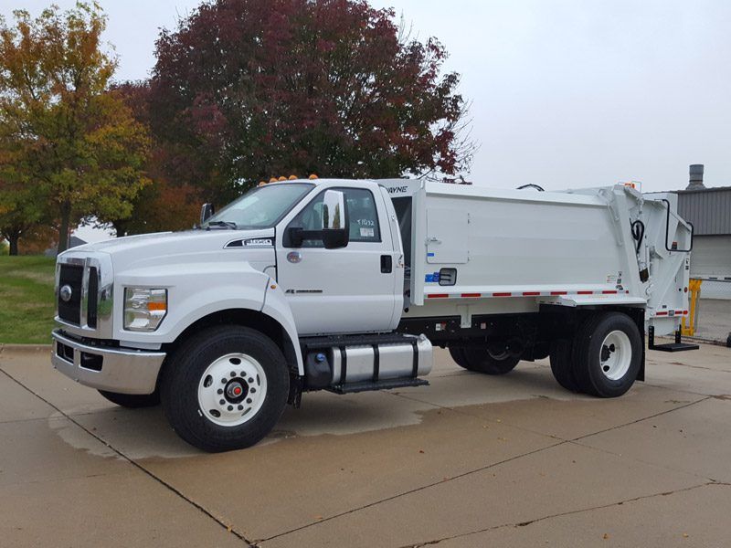 White utility dump truck parked on wet pavement with autumn trees in the background