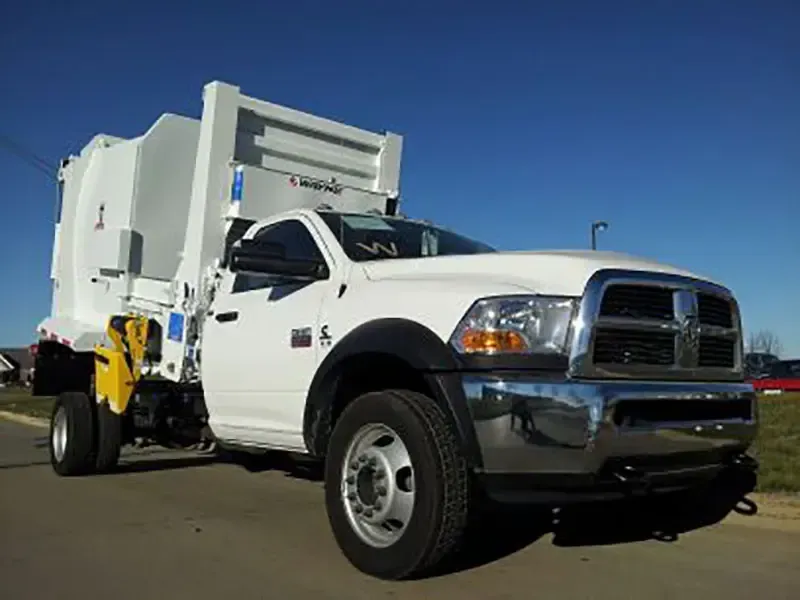 White utility truck with rear-mounted trash compactor parked on a road under a clear blue sky