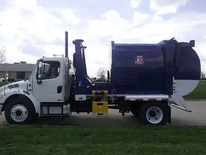 White-and-blue garbage truck parked on grass under a cloudy sky