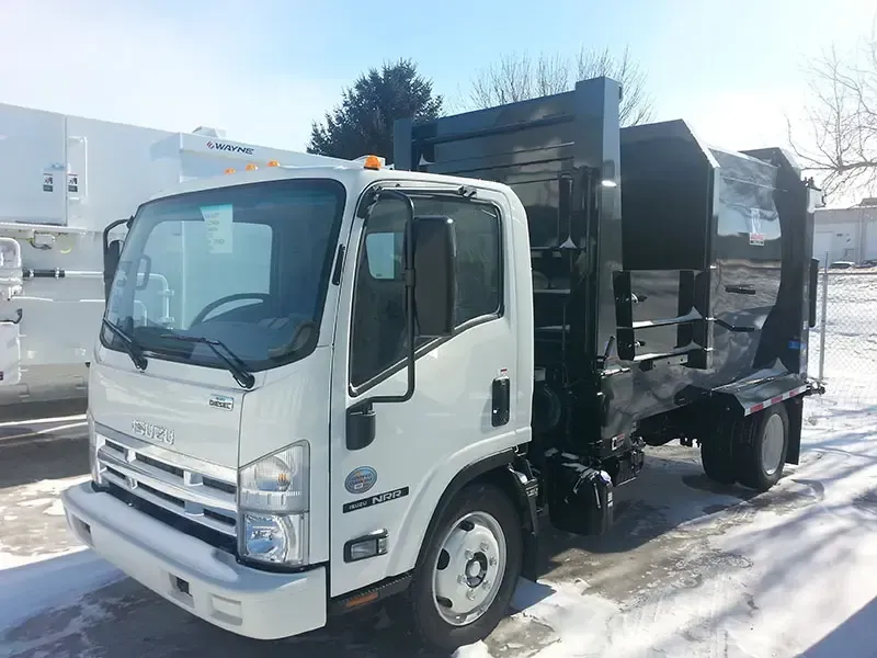 White dump truck parked on snow-covered ground in front of industrial buildings