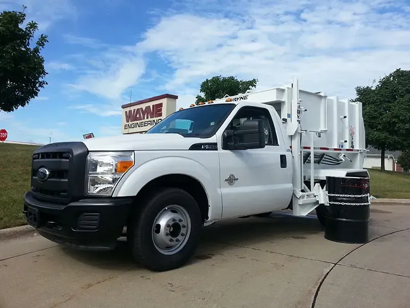 White garbage truck parked on a street beside a curb and trash can under a blue sky
