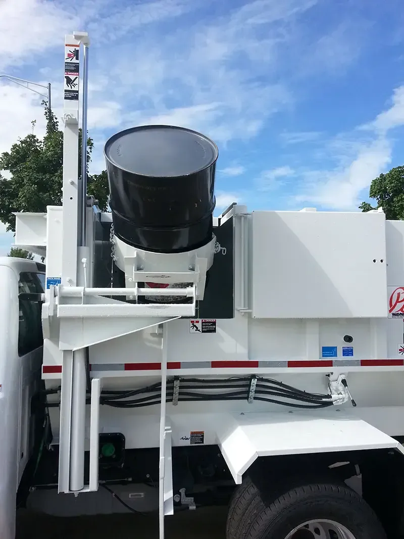 White utility truck with a large black cylindrical tank mounted on top, parked outdoors under a blue sky.