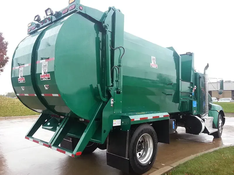 Green garbage truck parked on a wet road, rear view with large cylindrical compactor body