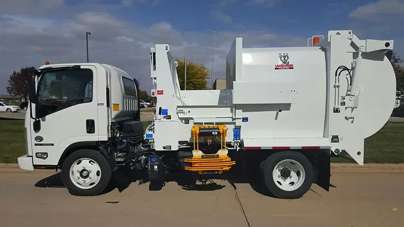White garbage truck with side loader parked on a street under a blue sky.