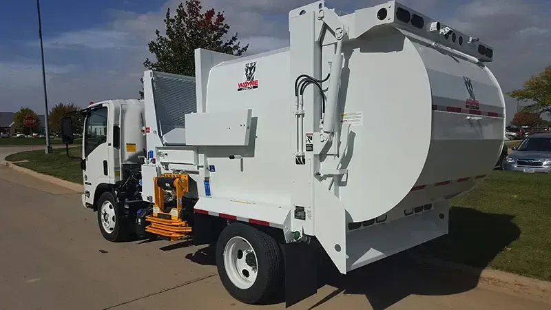 White garbage truck parked on a street, side loader arm visible on the passenger side.