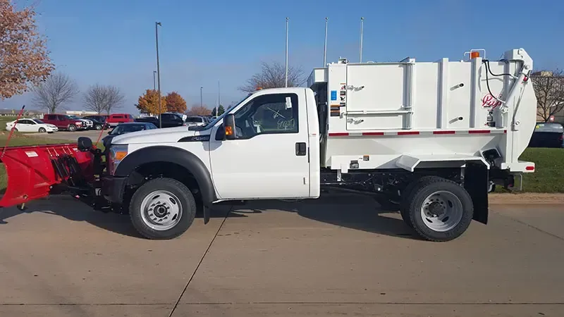 White utility truck with a red snowplow attached, parked outdoors on a sunny day.