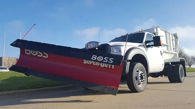 White pickup truck with a red-and-black snowplow parked on a sunny street.