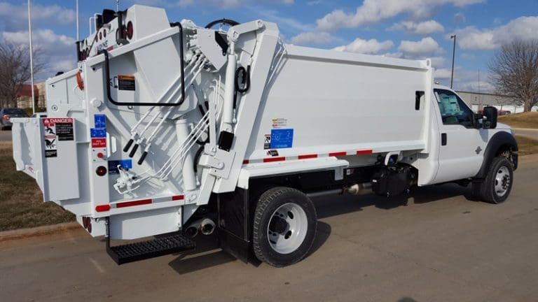 White utility truck with mounted rear equipment parked on a road under a cloudy sky