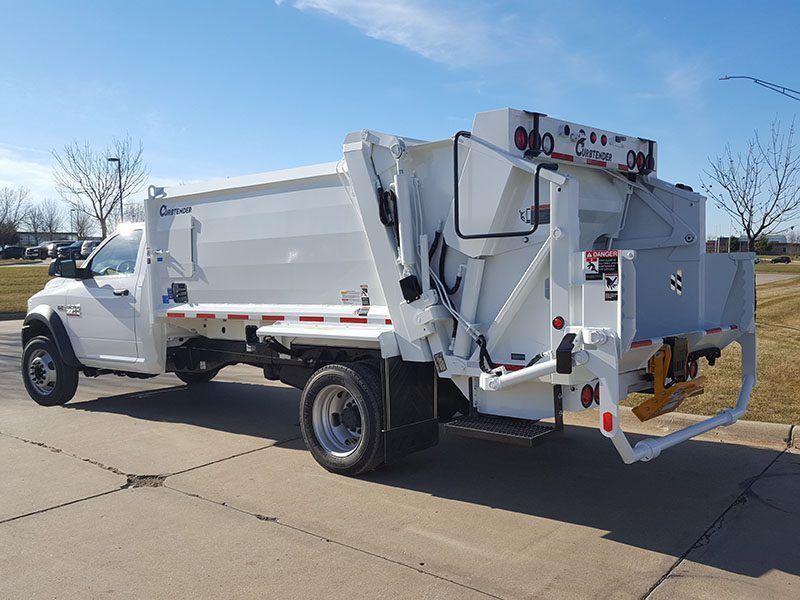 White garbage truck parked on a sunny street, side-loading mechanism visible.