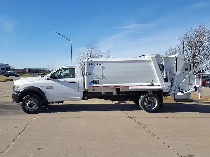 White garbage truck parked on a sunny road beside a sidewalk, side view.