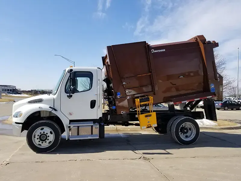 White dump truck with brown dumpster body parked on a sunny lot under a blue sky