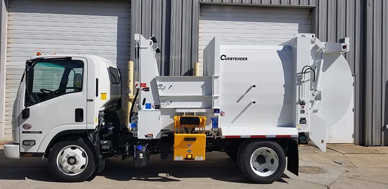 Side view of a white garbage truck parked beside a warehouse loading dock