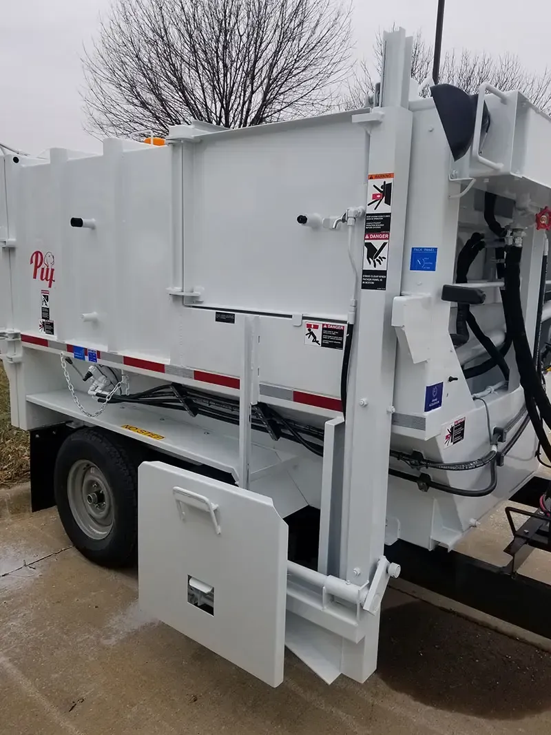 White industrial truck with rear compactor on a wet street, side access door open