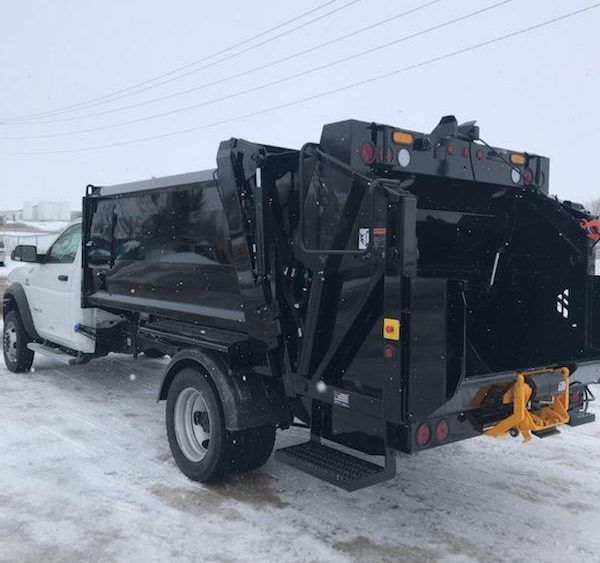 Black garbage truck on a snowy street, side view with white cab and rear hopper attached
