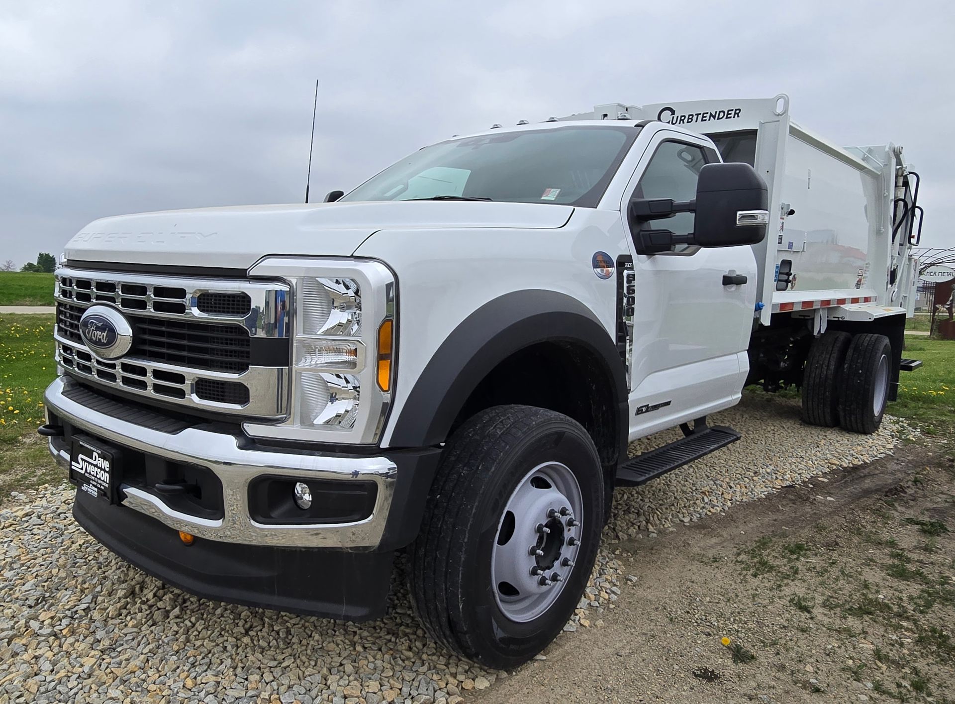 White Ford dump truck parked on a gravel lot under cloudy sky