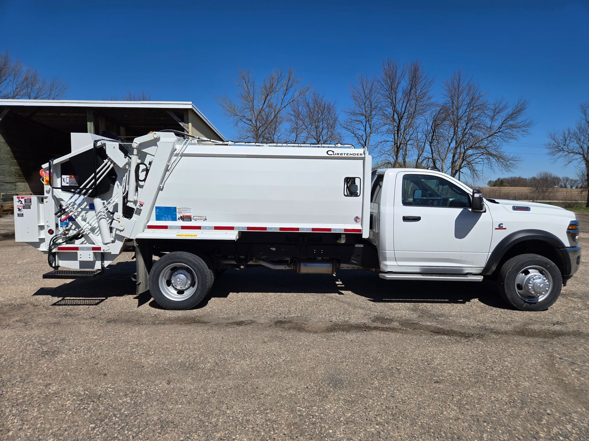 White utility truck with a rear-mounted lift or equipment, parked on a gravel lot under a clear blue sky