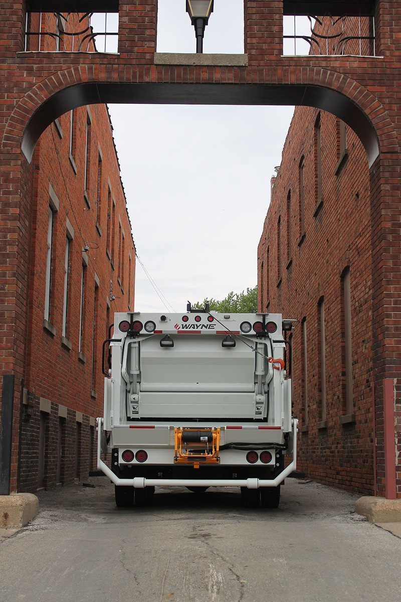 White utility truck parked in a narrow alley between brick buildings under an overhead arch.