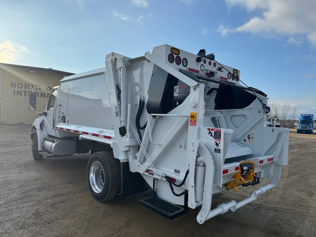White garbage truck parked outdoors on a sunny day, side loading mechanism visible.