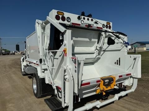 White garbage truck parked outdoors, rear view with hydraulic lifting arms and orange safety hardware