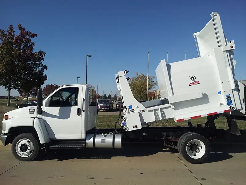 White commercial truck with a garbage lift bed parked outdoors on a sunny street.
