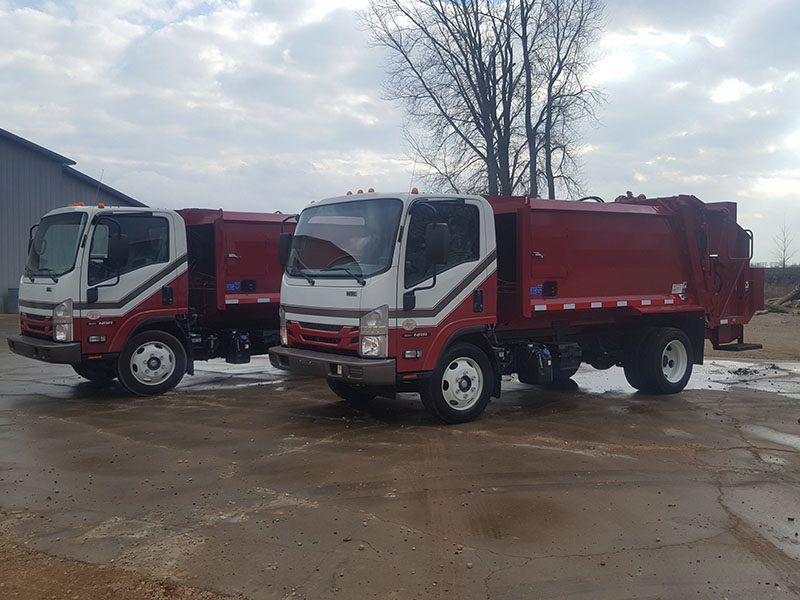 Two red-and-white dump trucks parked on a wet lot under a cloudy sky