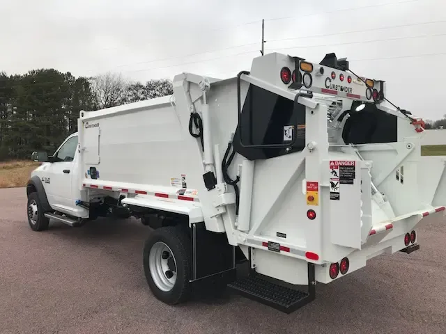 White utility truck with rear lift gate parked on a road under an overcast sky