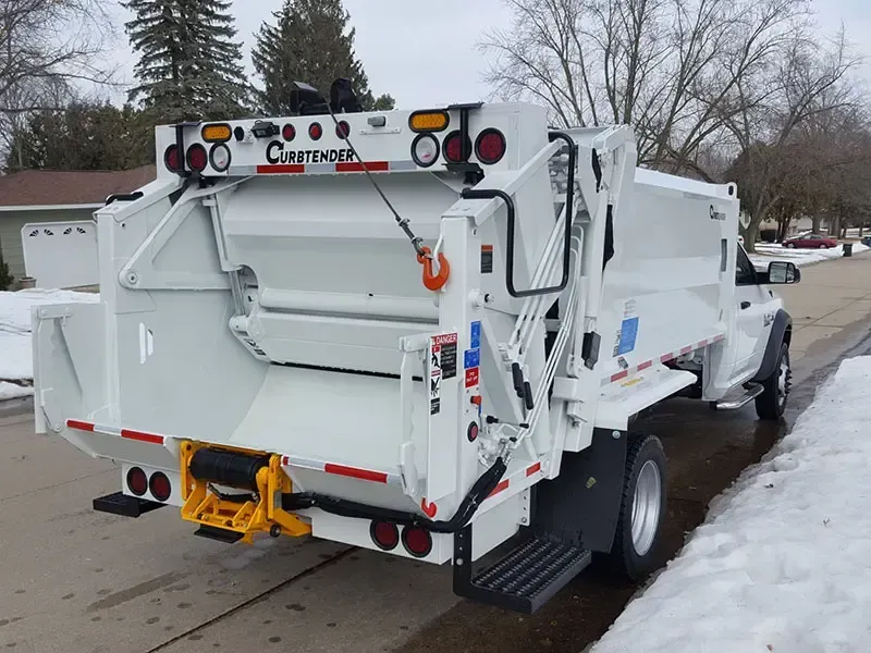 Rear view of a white garbage truck parked on a snowy street, with a city logo on the back.