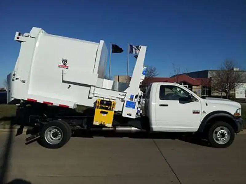 White garbage truck with rear loader parked on a street under a clear blue sky