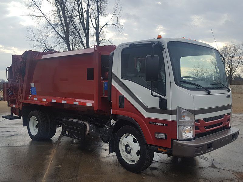 Red-and-white garbage truck parked on a wet street under a cloudy sky
