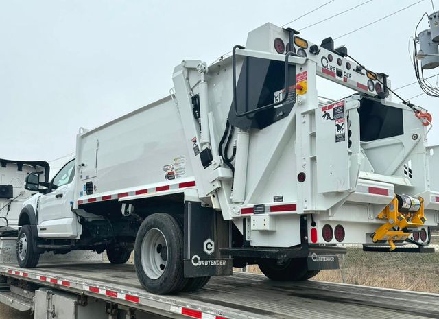 White dump truck on a flatbed trailer in a snowy outdoor work yard