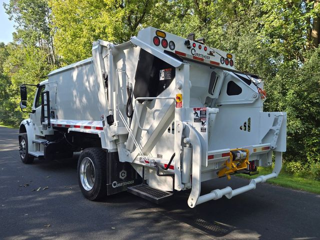 White garbage truck on a tree-lined road with the rear loading mechanism visible