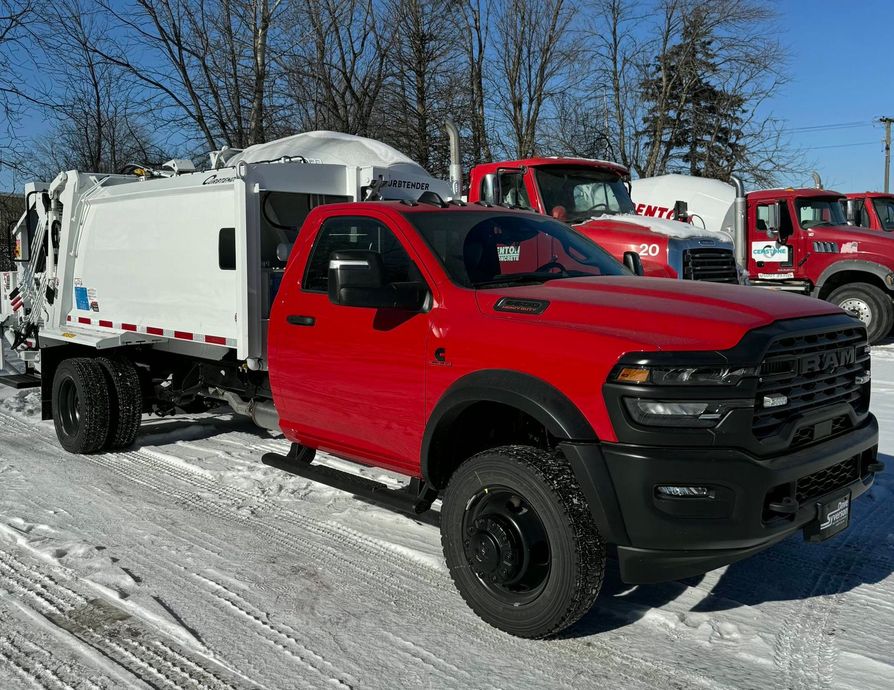 Red pickup truck with a white utility bed parked in a snowy lot beside other trucks.