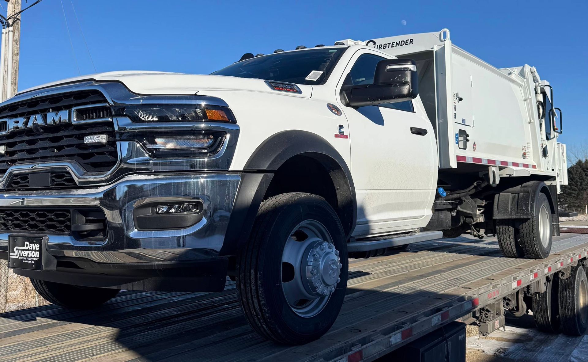 White heavy-duty pickup truck on a flatbed trailer, viewed from the front-left side.