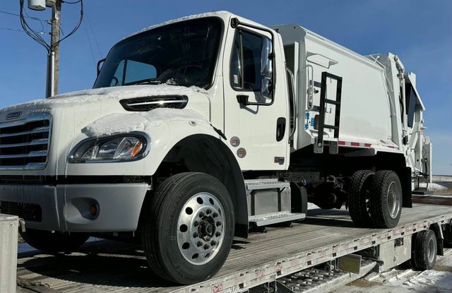 White garbage truck on a flatbed trailer in a snowy outdoor setting