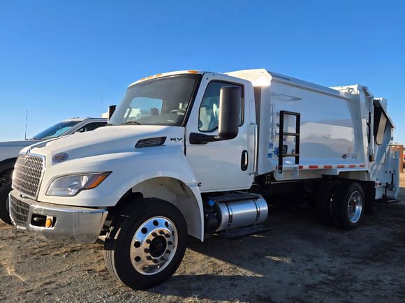 White garbage truck parked outdoors on a gravel lot under a clear blue sky