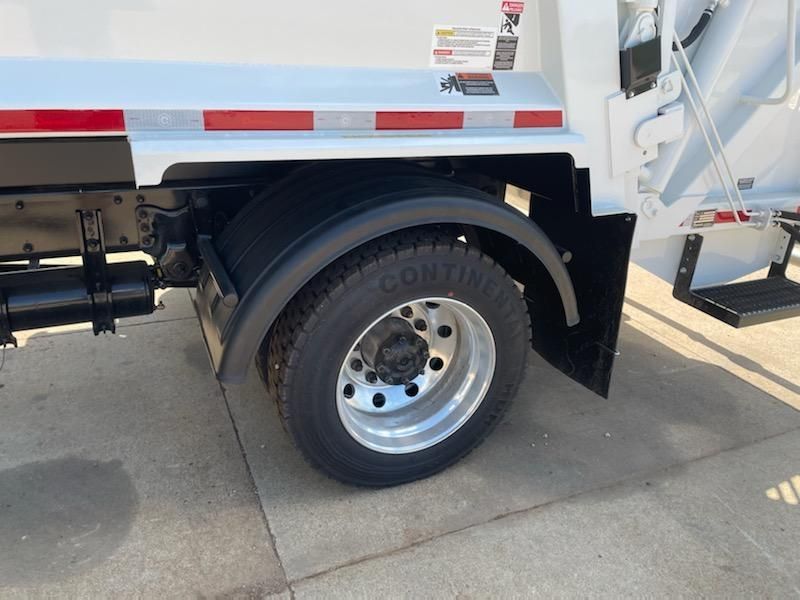 Close-up of a white truck’s rear wheel and fender on a sunlit pavement.