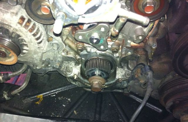 Close-up view of an exposed engine block with a central timing gear, alternator, and pulleys in a vehicle's engine bay. | Allstar Automotive
