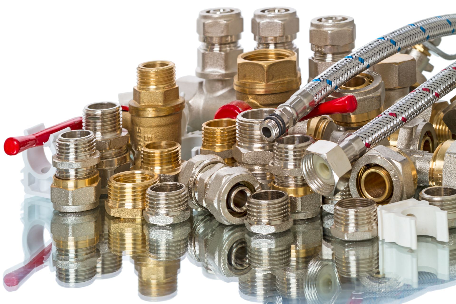 Assorted brass and metal plumbing fittings, valves, and flexible hoses arranged on a surface.