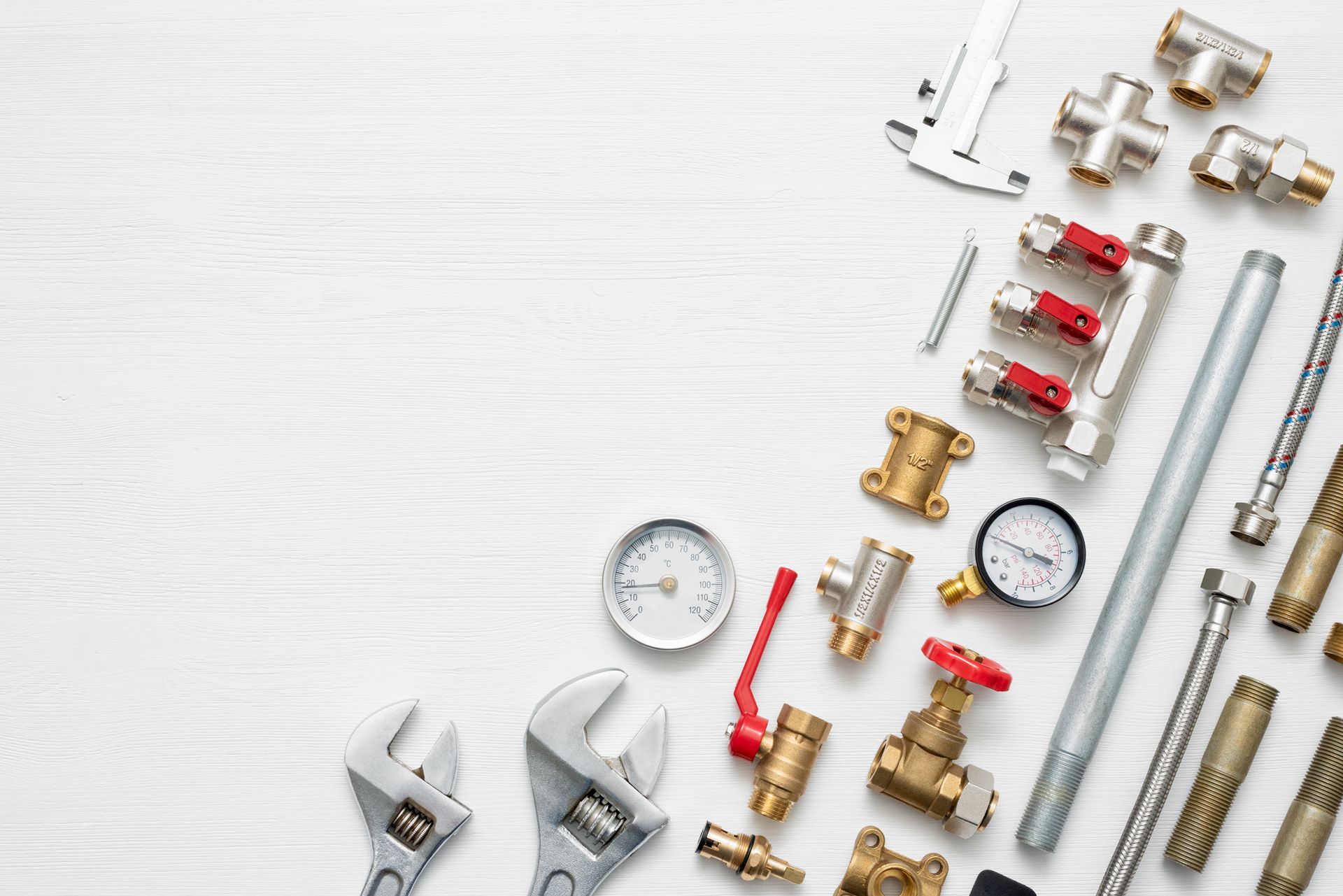 Plumbing tools with brass fittings and gauges arranged on a white wooden surface