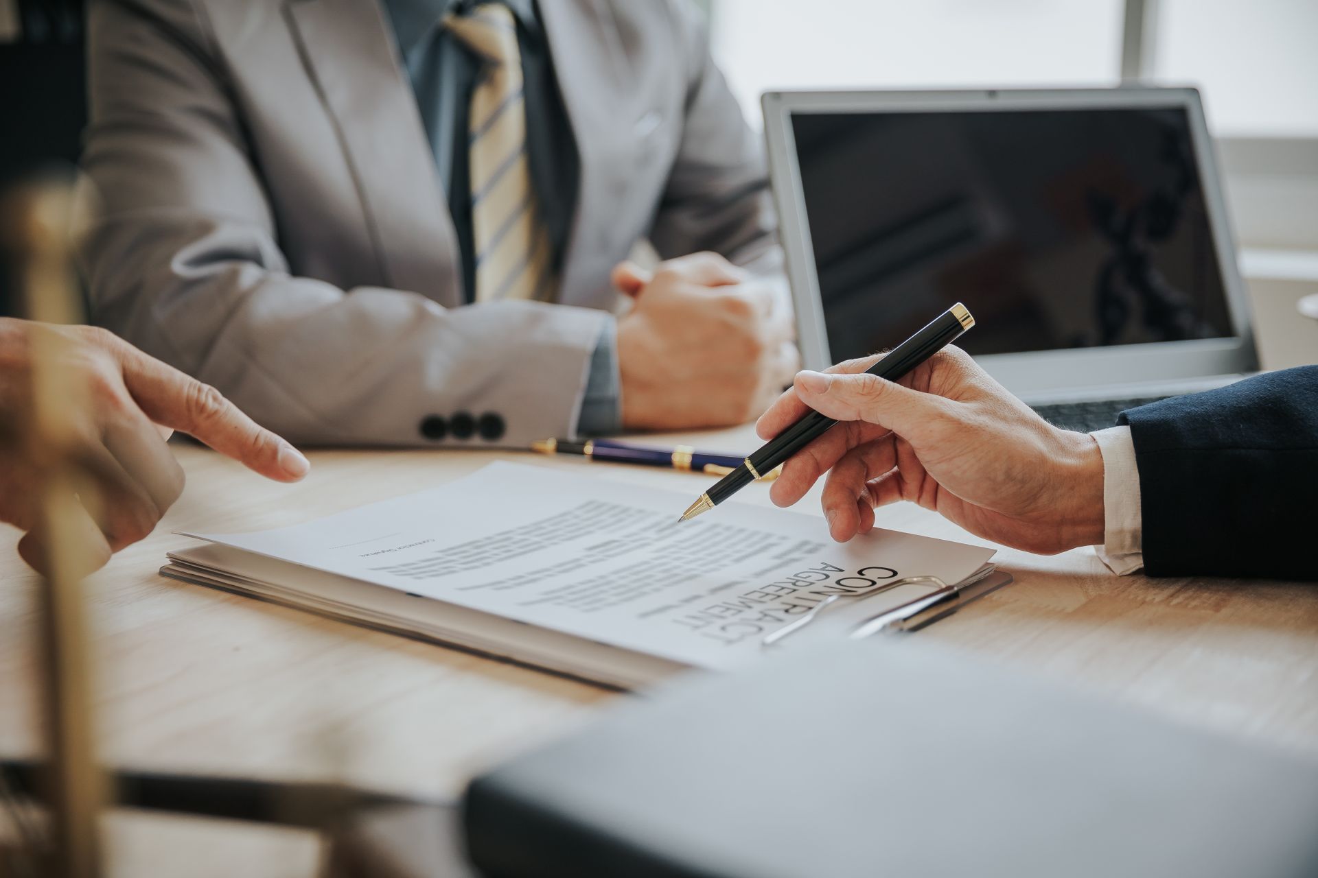 People in suits reviewing a document, one points, another holds a pen near it.