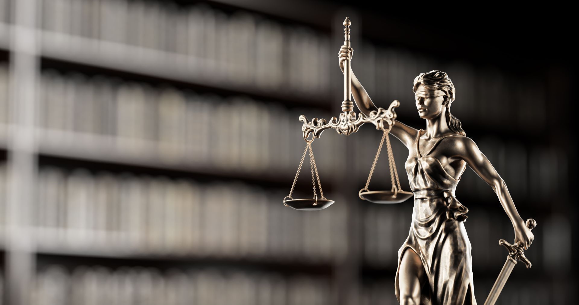 Statue of Lady Justice holding scales and sword, with blurred bookshelf background.