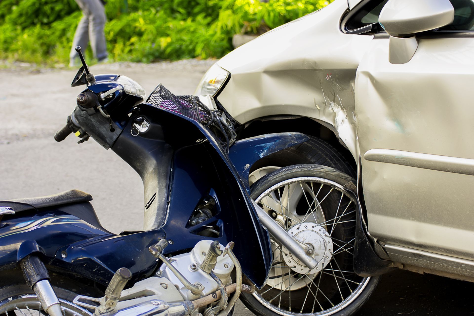 Motorcycle and car collision; damaged vehicles on a street. Blue motorcycle, silver car.